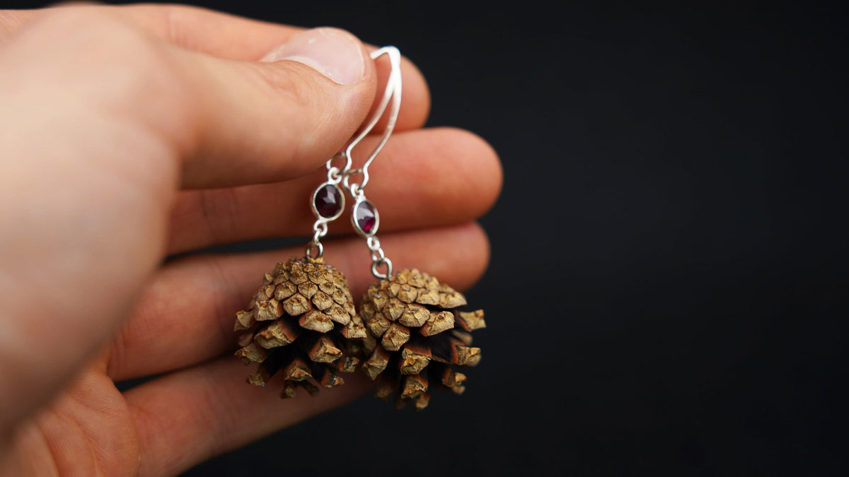 Kiefernzapfen-Ohrringe mit rotem Granat in 925 Silber in der Hand