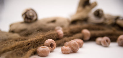 Roséfarbene Mondstein-Dreadlockperlen an Dreads vor Treibholz