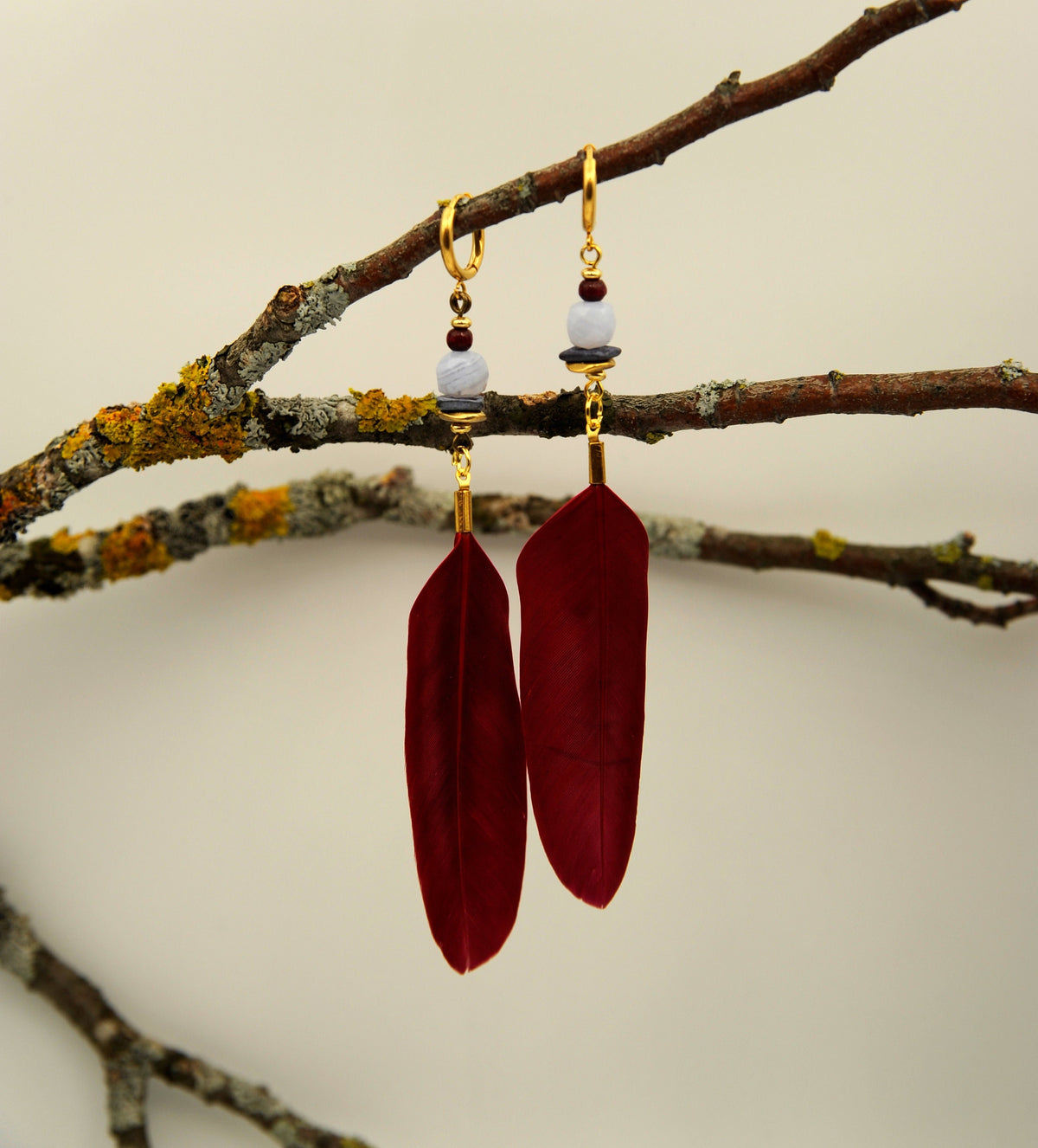 Rote Federohrringe aus Gänsefeder mit Chalcedon und goldenen Perlen an einem Ast